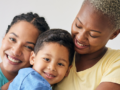 Two adult females hugging a child